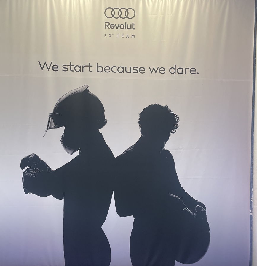 Plakat mit dem Schatten von zwei Rennfahrern mit Hel men bei der Audi Präsentation in Berlin im März 2026.